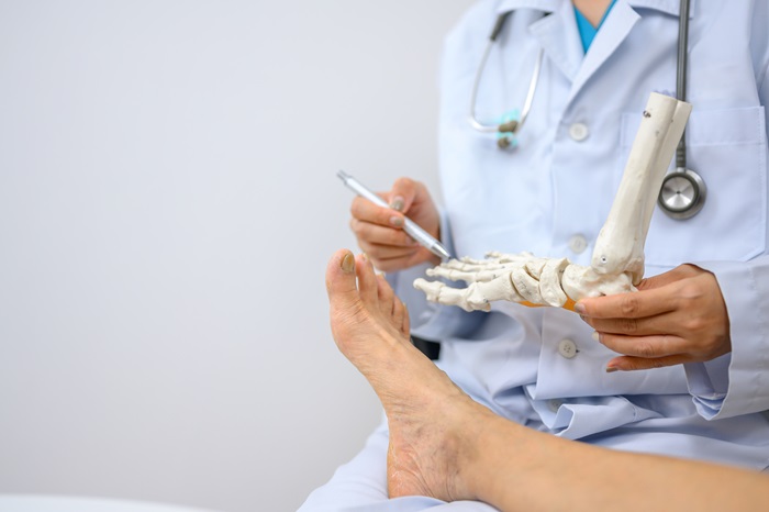 An orthopedic doctor holding a model of ankle and foot bones is explaining to a patient foot bone problems. Concept of health care for feet and foot bones
