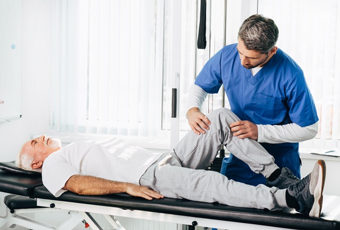 Pain doctor treating leg injury on a man lying down. Senior man training with his therapist. Joint, knee and leg pain treatment