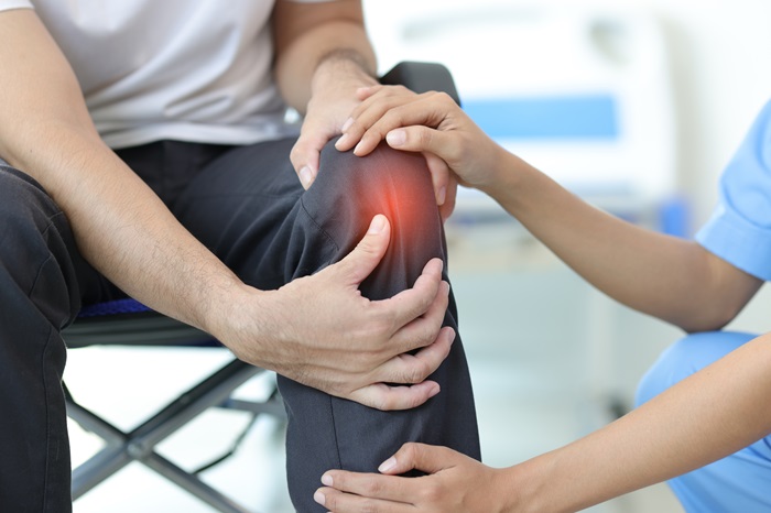 Doctor diagnosing knee pain of in examination room.