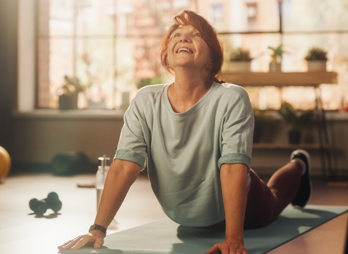 Healthy Athletic Fit Middle Aged Woman Training on a Yoga Mat, Doing Back Stretching and Core Strengthening Exercises During Morning Workout at Home in Sunny Apartment.