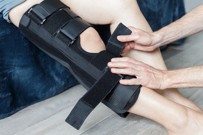 Closeup female leg in grey leggings dressed in knee brace to help promote recovery of bones, muscles, ligaments. Woman is feeling pain in joints after injury. Arthritis and meniscus diseases concept.