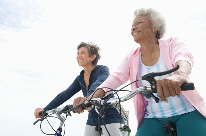 Low angle view of multiethnic senior female friends riding bicycles against sky